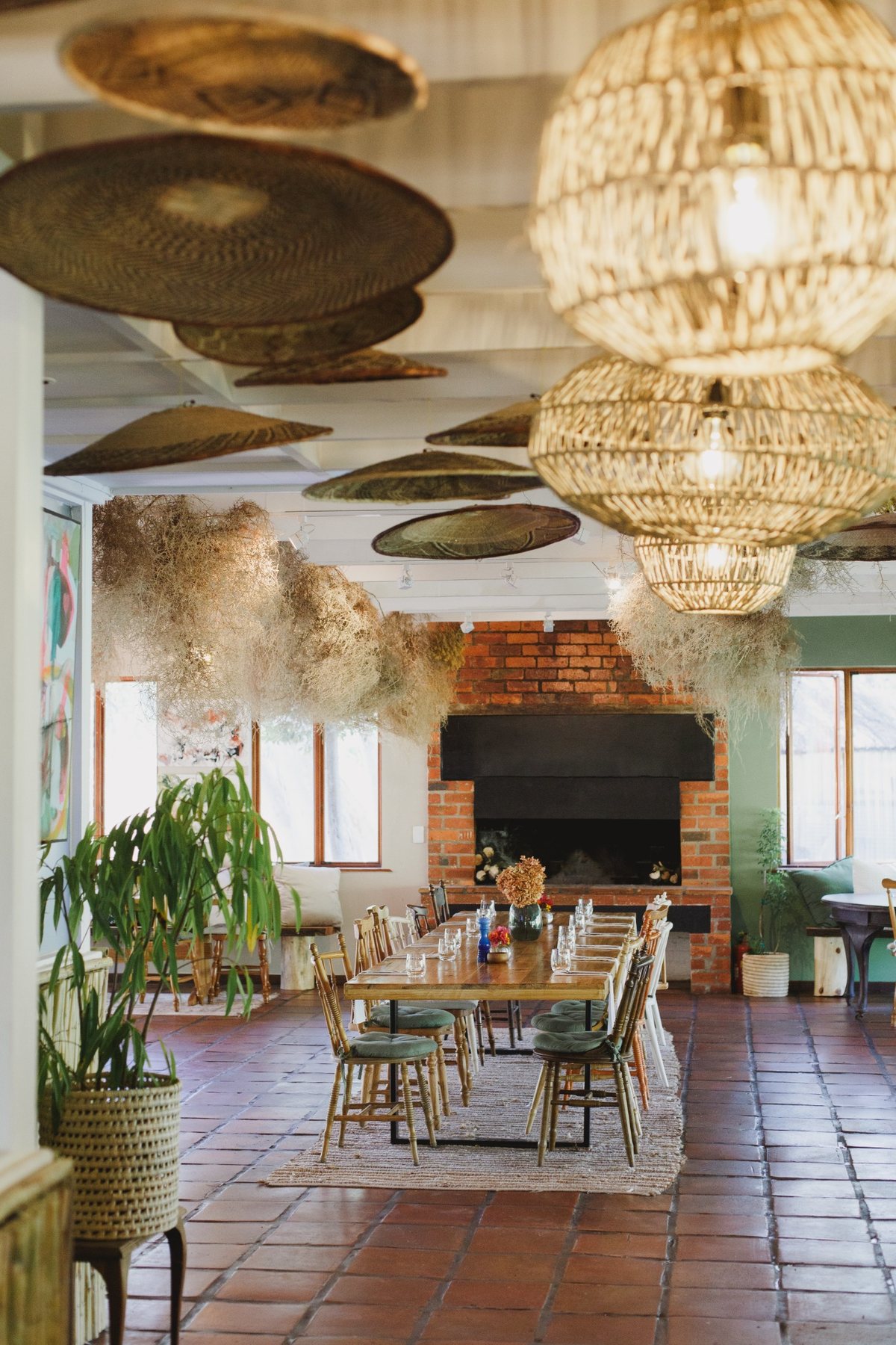A long dining table beneath woven baskets and pendant lights, with Melfort’s fireplace beyond